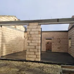 Wznoszenie ścian domu z pustaków ceramicznych Porotherm, widoczne nadproża betonowe i wylana posadzka parteru.