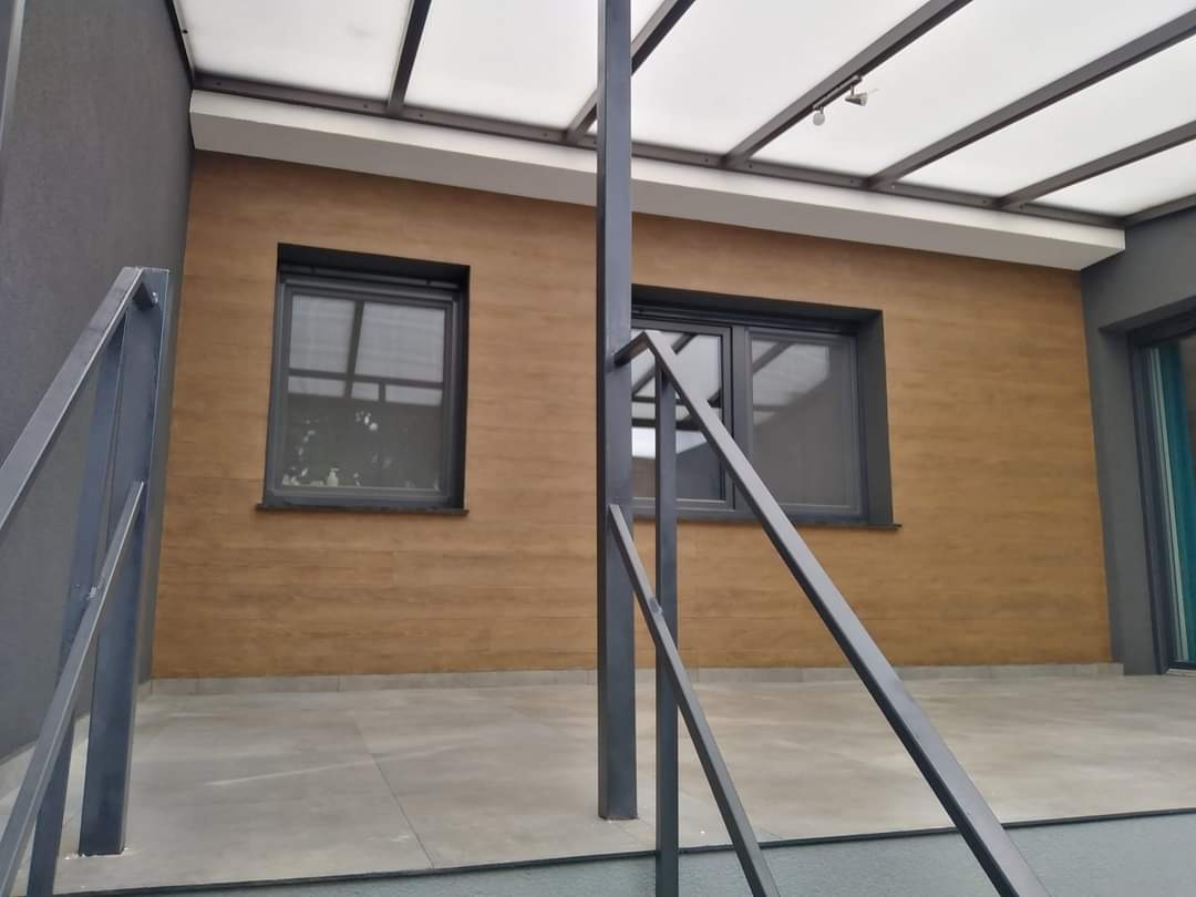 Nowoczesny dom z elewacją imitującą drewno, szare okna i metalowe balustrady schodów zewnętrznych.