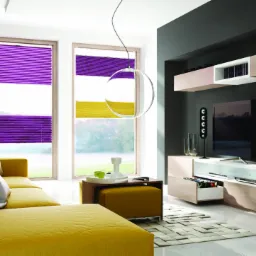 Jasny salon z żółtą sofą i plisami okiennymi w kolorze fioletowo-żółtym, oświetlony nowoczesną lampą wiszącą.