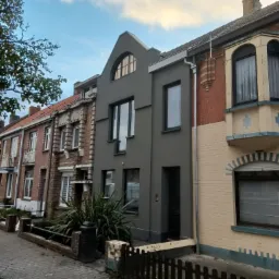 Ulica z szeregiem domów, w tym jeden z szarą, świeżo pomalowaną elewacją, wyróżniający się nowoczesnym wyglądem na tle tradycyjnej zabudowy z cegły.