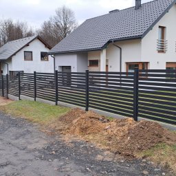 WK BLAST ECO - Nowoczesne, poziome ogrodzenie panelowe w kolorze antracytowym, zamontowane przy posesji w Żorach. Widoczny fragment ulicy i zaparkowany samochód dostawczy.