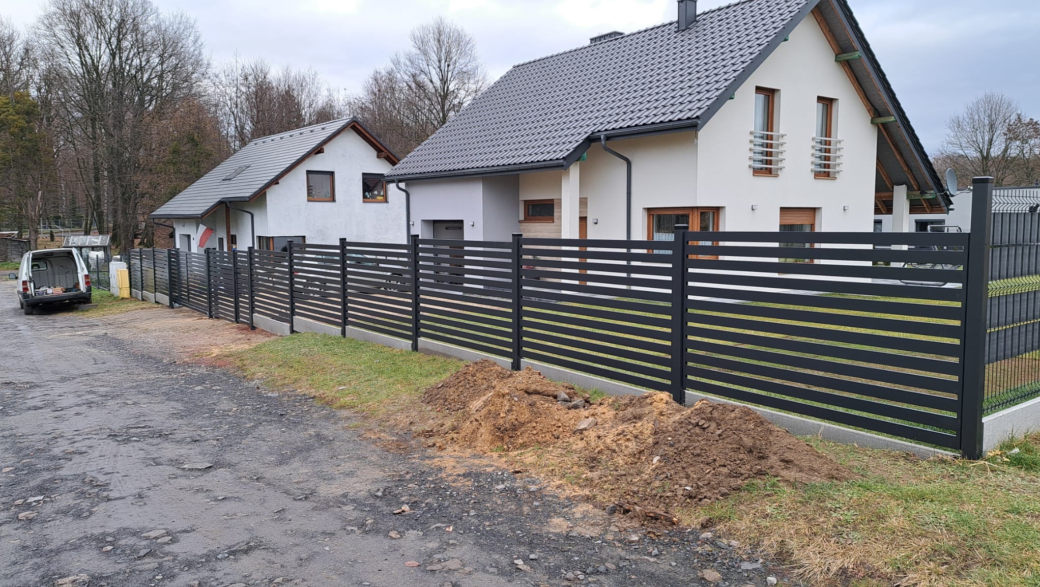 Nowoczesne, poziome ogrodzenie panelowe w kolorze antracytowym, zamontowane przy posesji w Żorach. Widoczny fragment ulicy i zaparkowany samochód dostawczy.