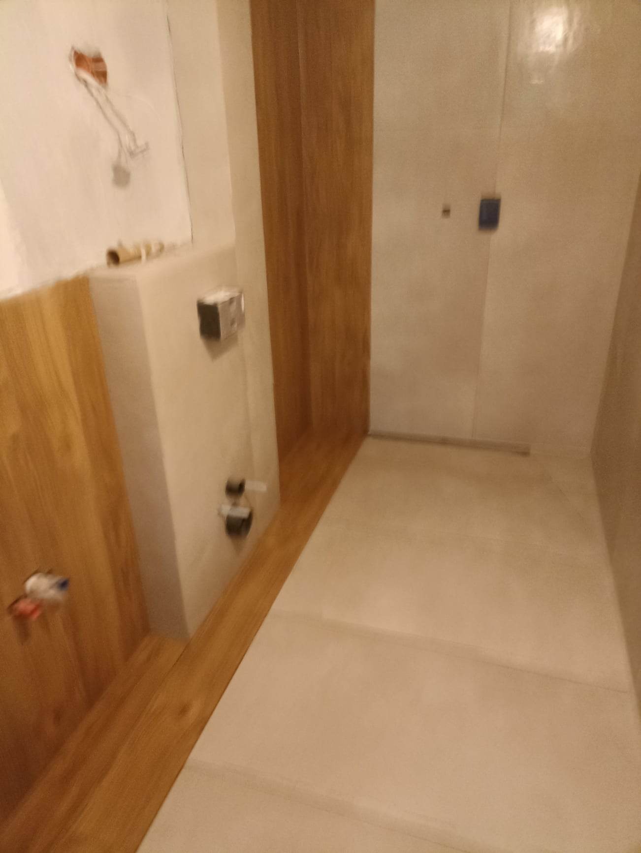 Wnętrze łazienki w trakcie wykańczania: ściany pokryte gładzią, częściowo obłożone panelami drewnopodobnymi, widoczne instalacje hydrauliczne przed montażem armatury.