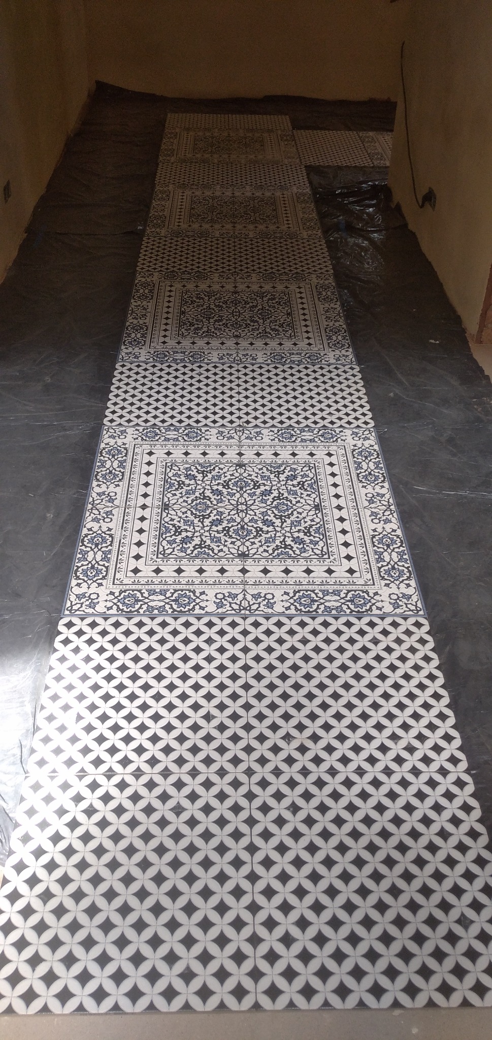 Układanie dekoracyjnych płytek podłogowych z motywem kwiatowym i geometrycznym w Płońsku, zabezpieczone folią podłoże.