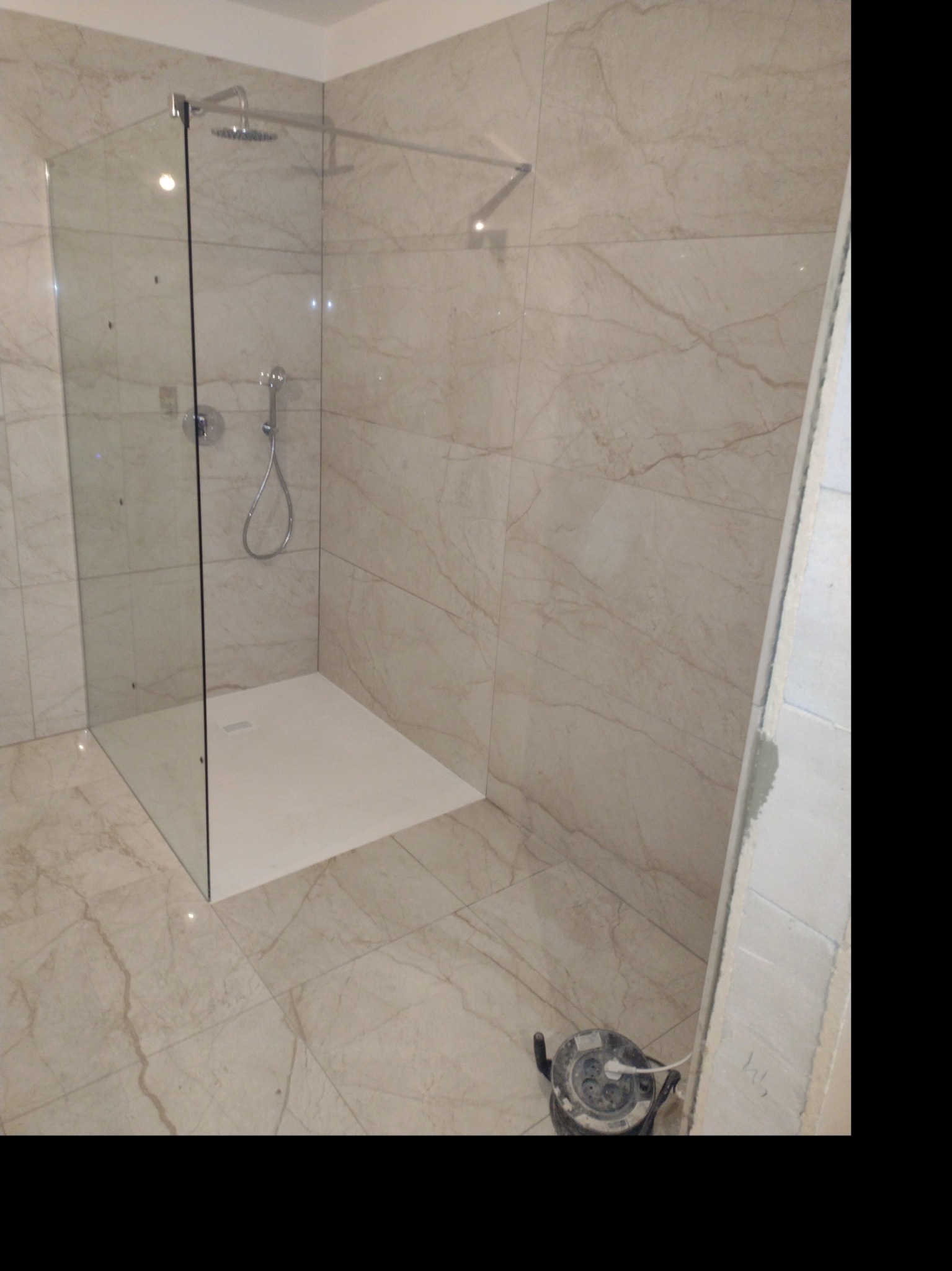 Nowoczesna kabina prysznicowa typu walk-in z deszczownicą, wykończona płytkami imitującymi marmur, z widocznym przedłużaczem na podłodze.