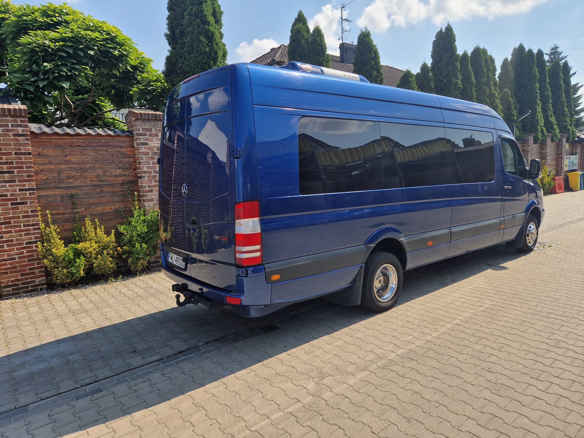 Niebieski bus Mercedes Sprinter 519 CDI zaparkowany na brukowanej nawierzchni, widok z tyłu, z hakiem holowniczym i chromowanymi kołpakami.