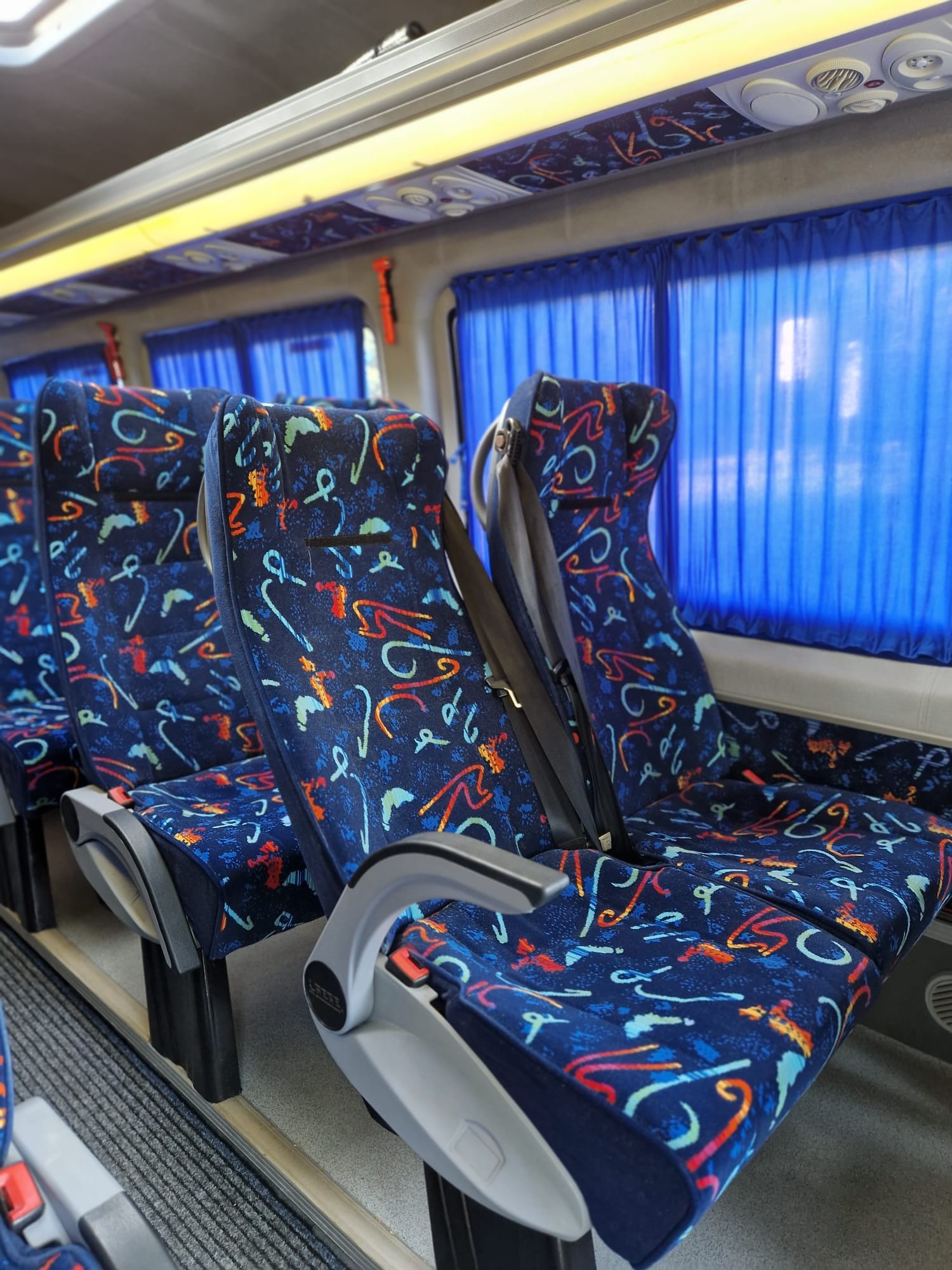 Wnętrze autobusu z rzędami niebieskich foteli w abstrakcyjne wzory i zasłonami w oknach