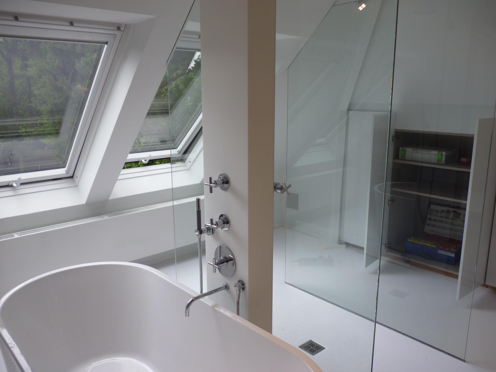 Nowoczesna, minimalistyczna łazienka z owalną wanną, szklaną kabiną prysznicową i oknami dachowymi, widok na zieleń za oknem.