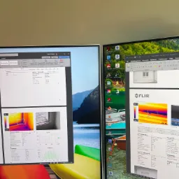 Dwa monitory wyświetlają analizę termowizyjną okna, z programem FLIR Thermal Studio pokazującym obrazy termiczne i profile temperatur, otoczenie biurowe.