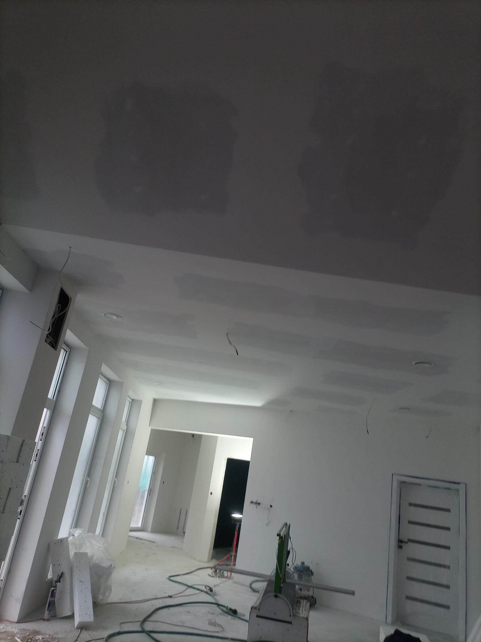 Wnętrze w trakcie remontu: widoczne szpachlowane łączenia płyt kartonowo-gipsowych na suficie, narzędzia do cięcia profili, oraz wstępnie przygotowane ściany, z widocznymi przewodami elektrycznymi.