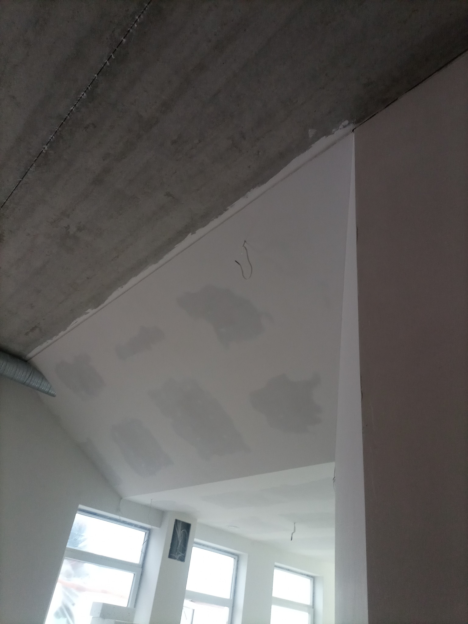 Sufit pod skosem z widocznymi śladami po szpachlowaniu, przygotowany do malowania, z surowym betonem powyżej i widocznymi przewodami elektrycznymi.