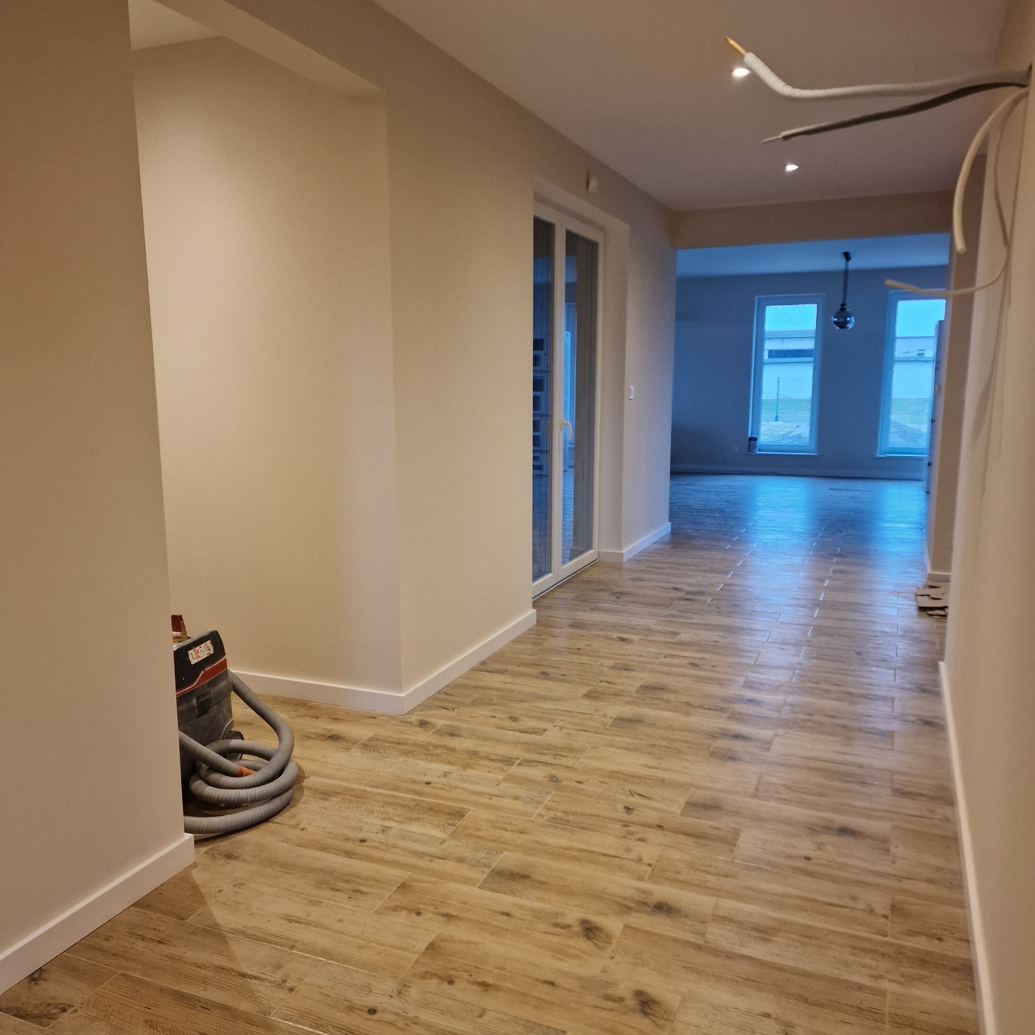 Korytarz po remoncie w Inowrocławiu: ułożone płytki imitujące drewno, pomalowane ściany, widoczne kable i odkurzacz. Prace wykończeniowe w trakcie.