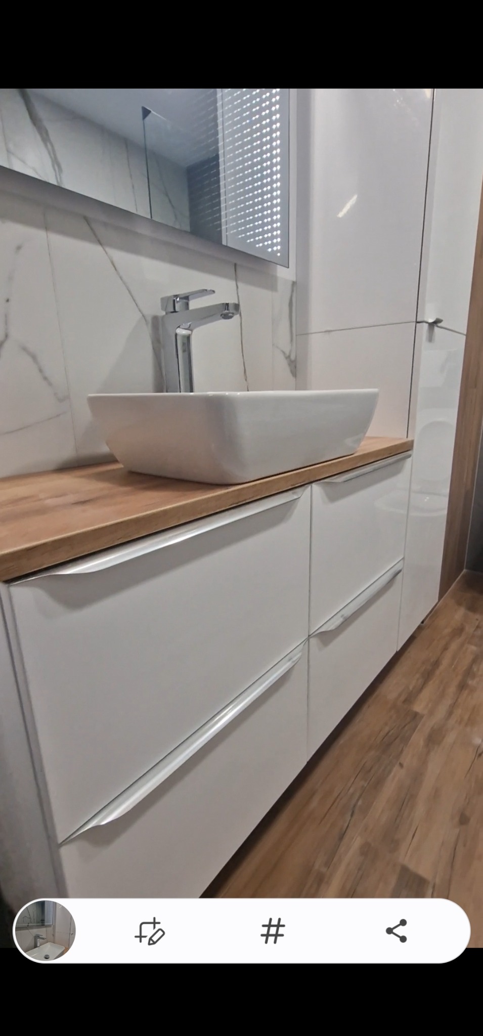 Nowoczesna łazienka: biała szafka pod umywalkę z drewnianym blatem, kwadratowa umywalka i bateria. Na ścianie marmurowe płytki i lustro z podświetleniem.