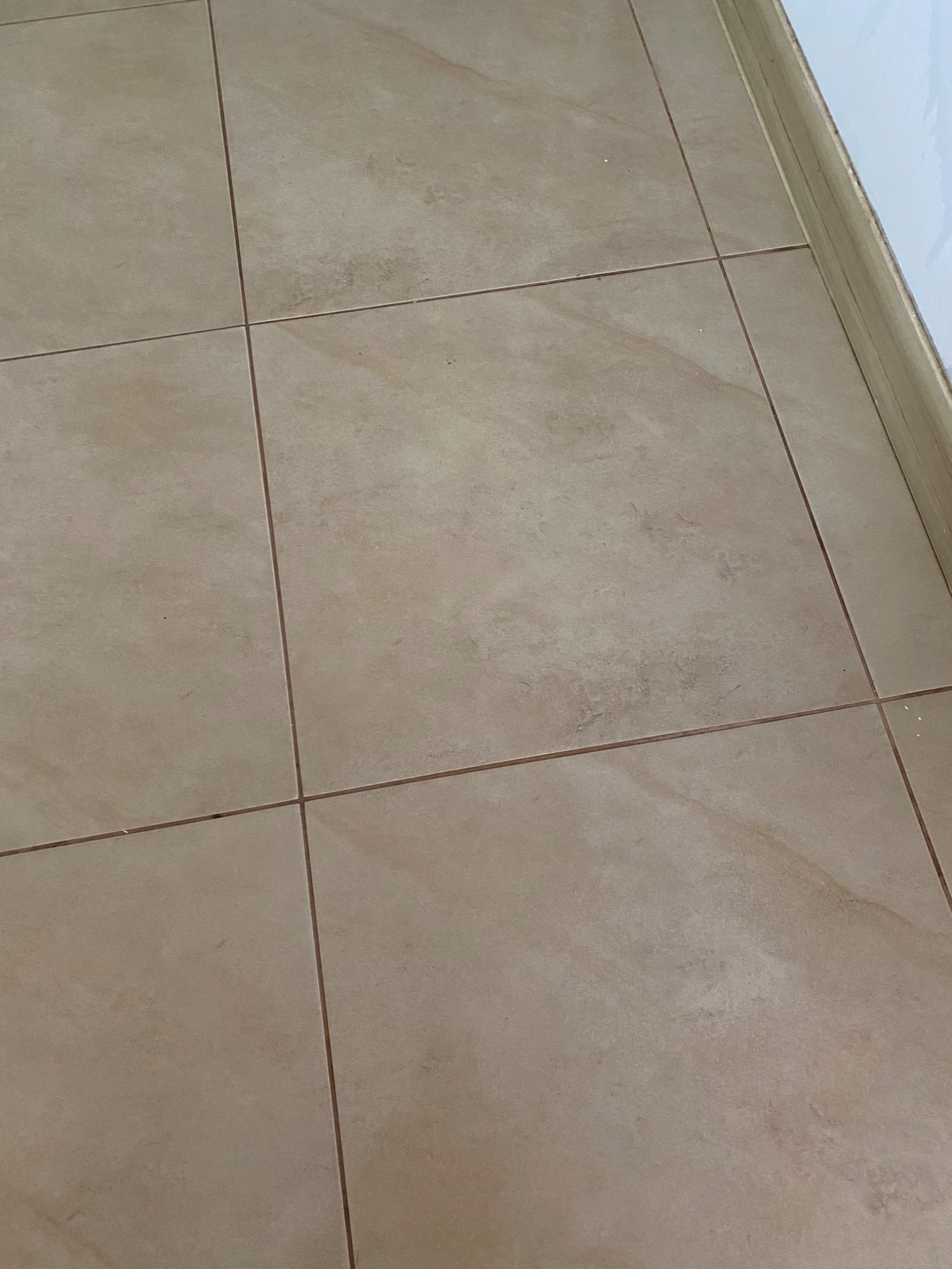 Beżowe płytki podłogowe z widocznymi fugami i listwą przypodłogową, ukazujące regularny wzór i fakturę materiału.