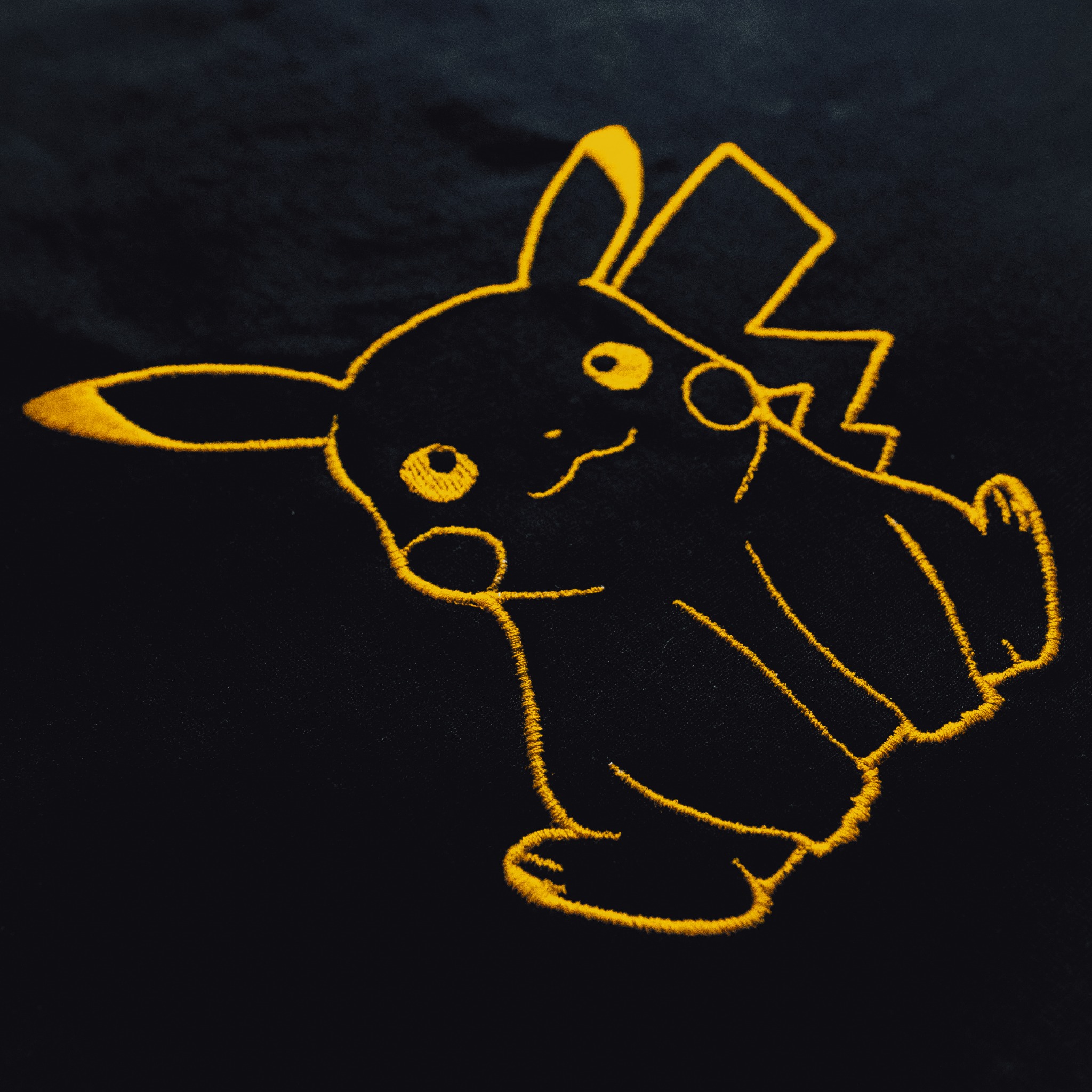 Żółty haft konturowy Pikachu na czarnym materiale.