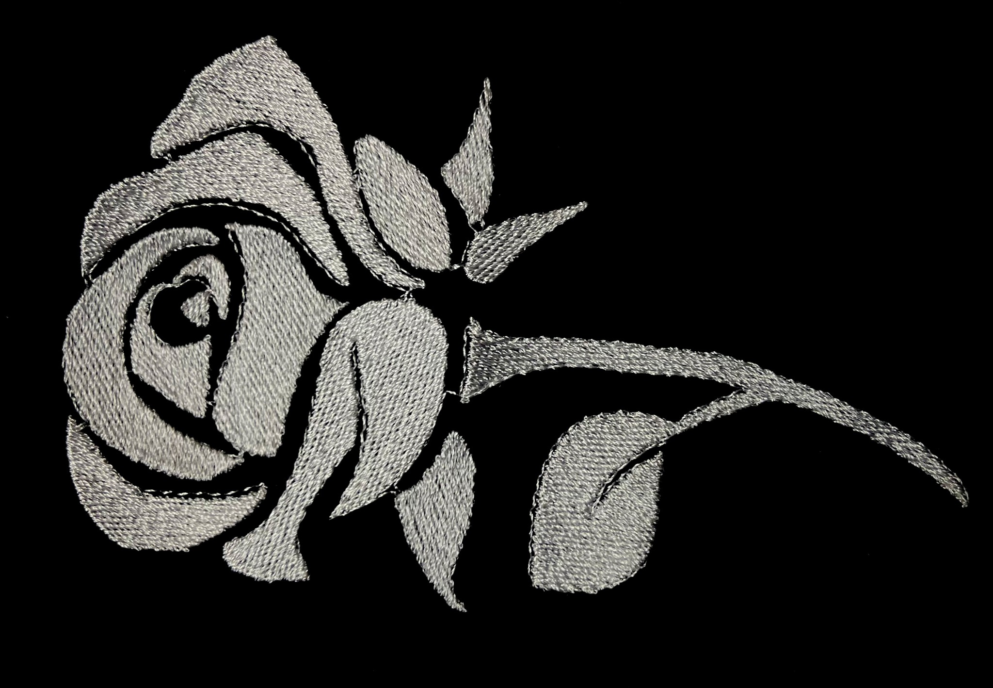 Delikatny, srebrny haft przedstawiający stylizowaną różę na czarnym tle.