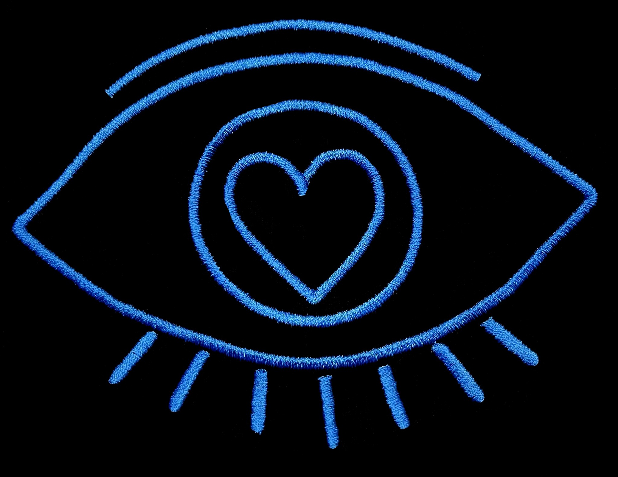 Niebieski haft przedstawiający oko z sercem w źrenicy, na czarnym tle.