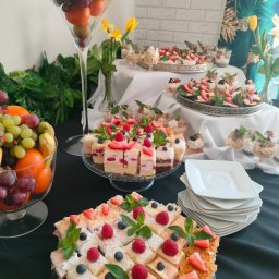NALEŚNIKARNIA ANCYMONEK Małgorzata Wójcik - Stół cateringowy z różnorodnymi deserami: mini torciki z truskawkami i borówkami, desery w szklankach, owoce w wazonach, dekorowany kwiatami i zielenią.