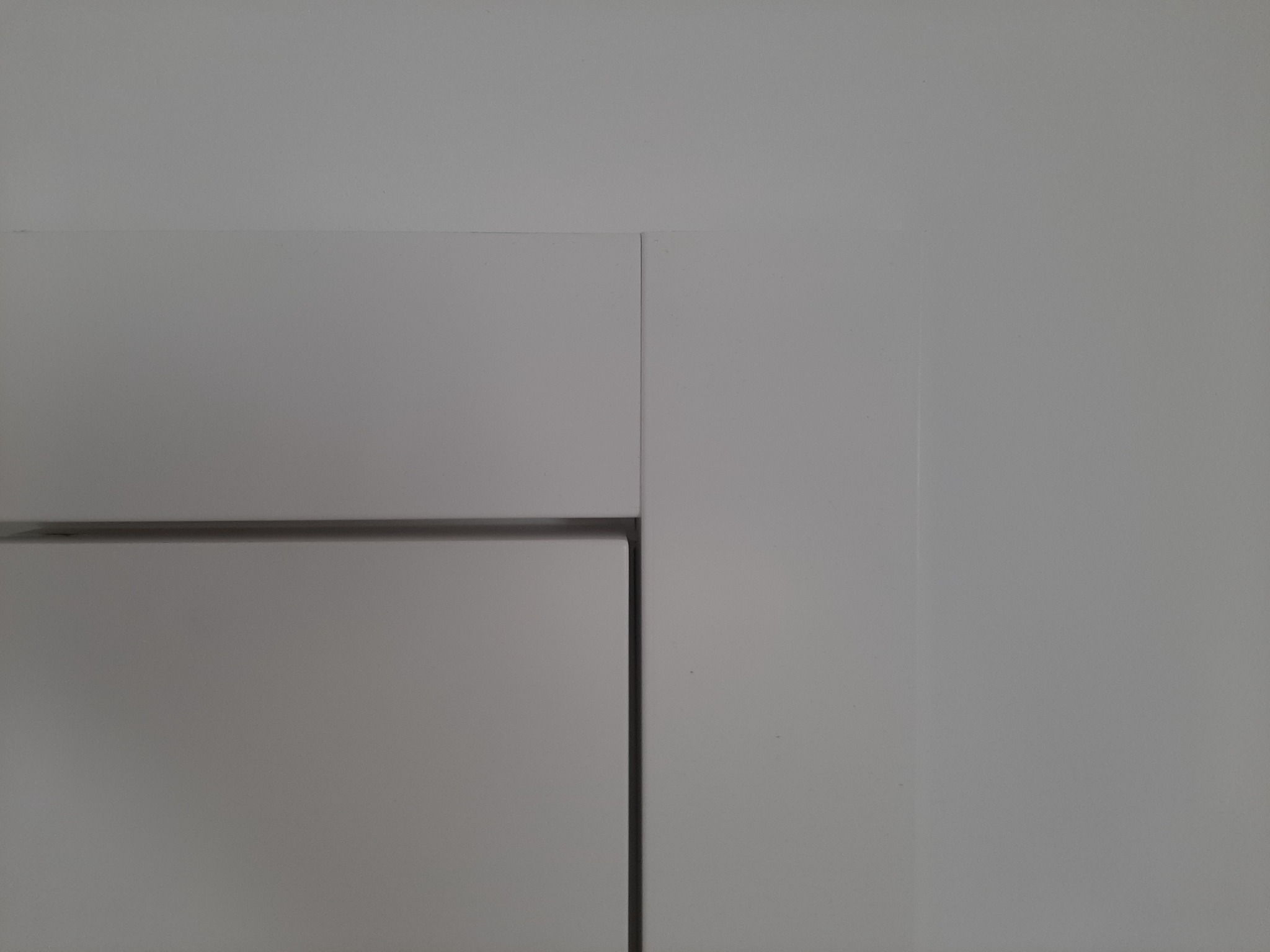 Fragment białej, minimalistycznej szafki z widocznymi krawędziami i subtelnym cieniem, ukazujący precyzję wykonania.