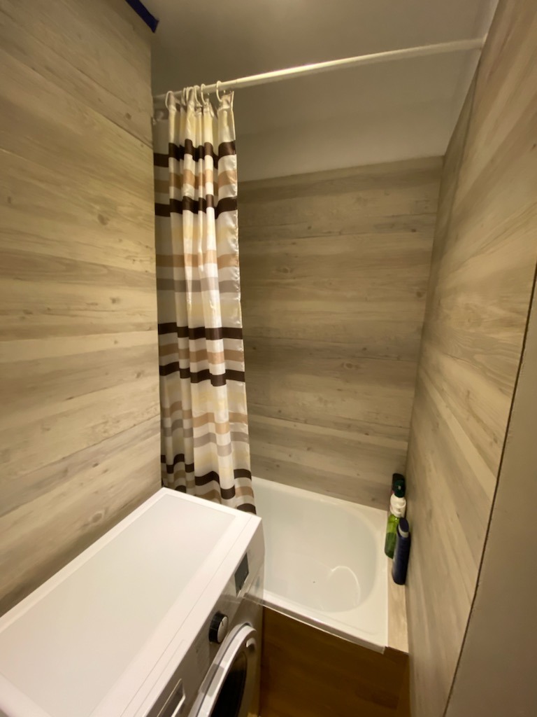 Łazienka z wanną, zasłoną w paski, pralką i ścianami wykończonymi panelami imitującymi drewno.