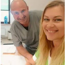 Uśmiechnięci lekarze w uniformach, selfie w gabinecie z dokumentami na biurku.