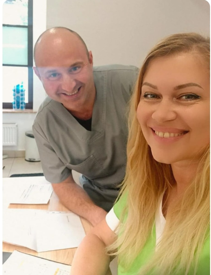 Uśmiechnięci lekarze w uniformach, selfie w gabinecie z dokumentami na biurku.