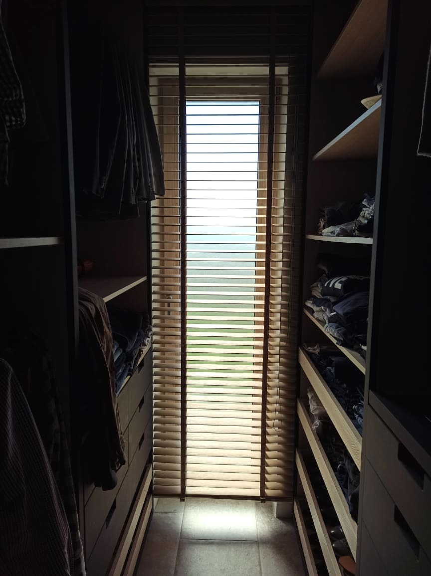 Wnętrze garderoby z drewnianymi żaluzjami poziomymi w oknie, wpadające światło słoneczne.