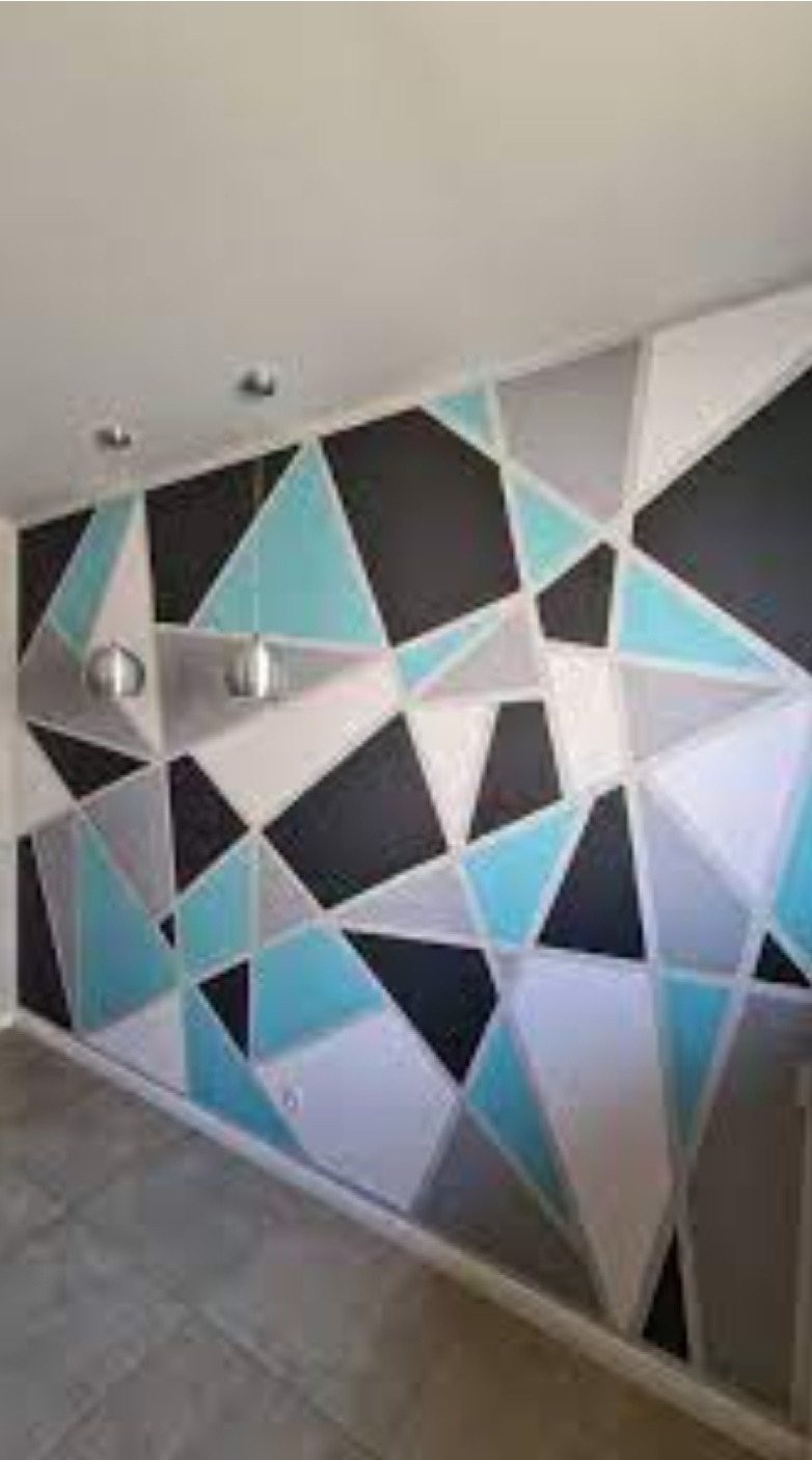 Ściana z geometrycznym wzorem w odcieniach czerni, szarości, bieli i turkusu, oświetlona dwoma metalowymi lampami sufitowymi.