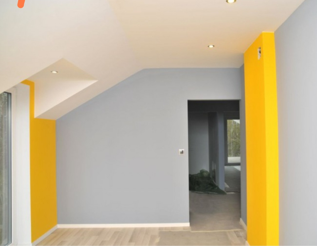 Pomalowane na szaro i żółto wnętrze z widocznymi punktowymi lampami sufitowymi i otwartym przejściem do kolejnego pomieszczenia.