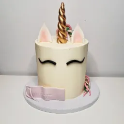 Tort jednorożec z kremowym lukrem, złotym rogiem i uszami z różowym detalem, z imieniem 'Kinga' na różowej wstążce.