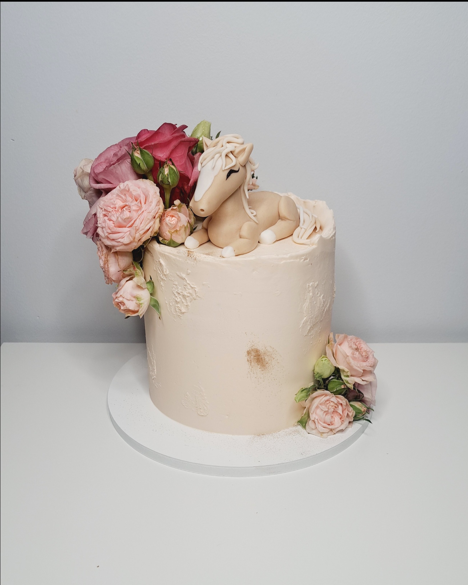 Tort ozdobiony kremem, różami i figurką leżącego konika z lukru.
