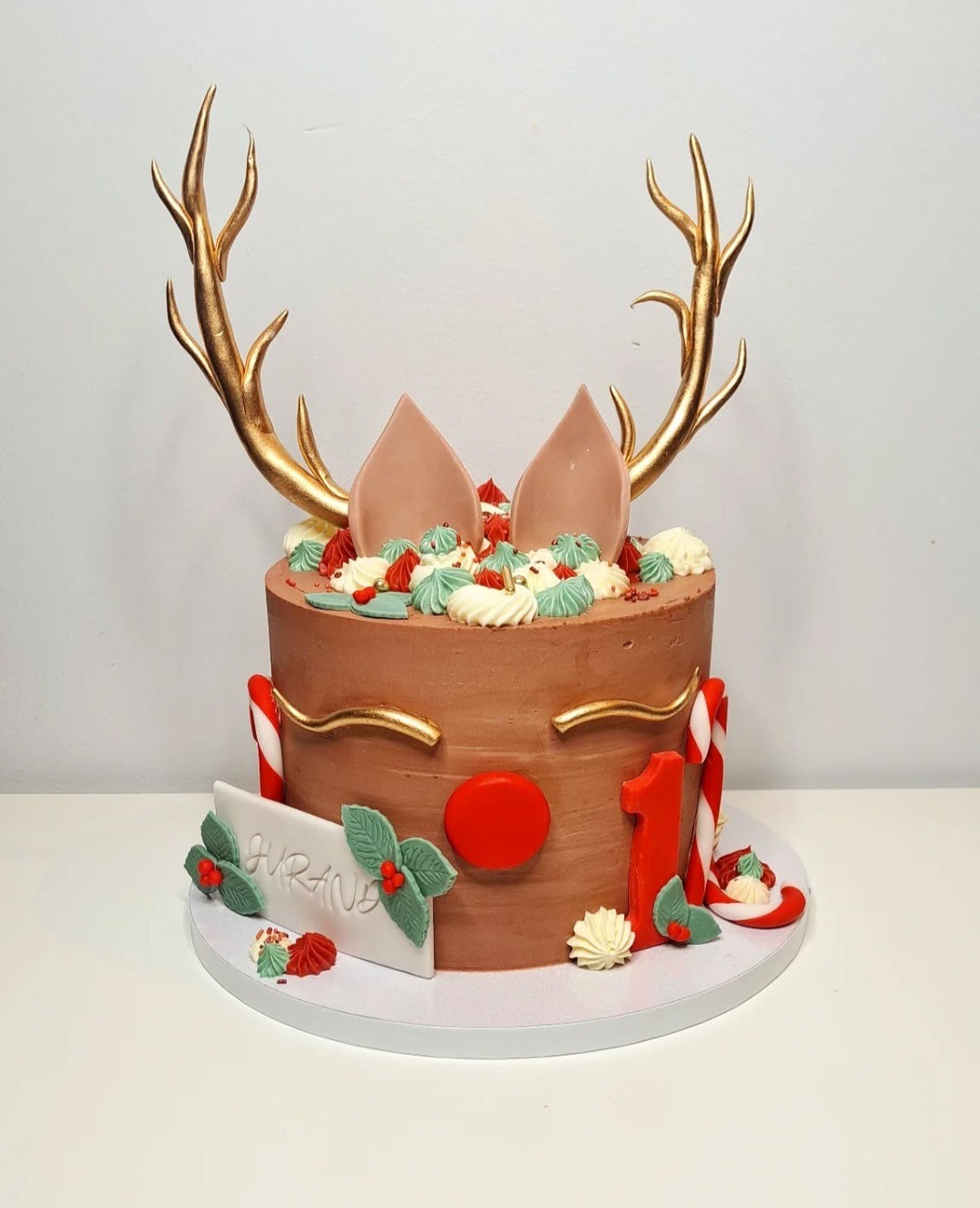 Urodzinowy tort w stylu renifera z czekoladowym kremem, złotymi rogami i uszami, dekorowany świątecznymi elementami i napisem 'Jurand'.