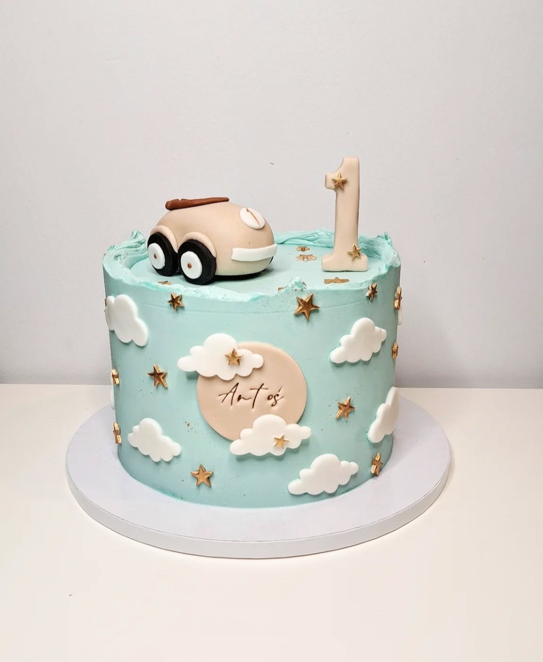 Tort urodzinowy dla roczniaka w pastelowych kolorach z dekoracjami z masy cukrowej: autko, chmurki, gwiazdki i cyfra '1'.