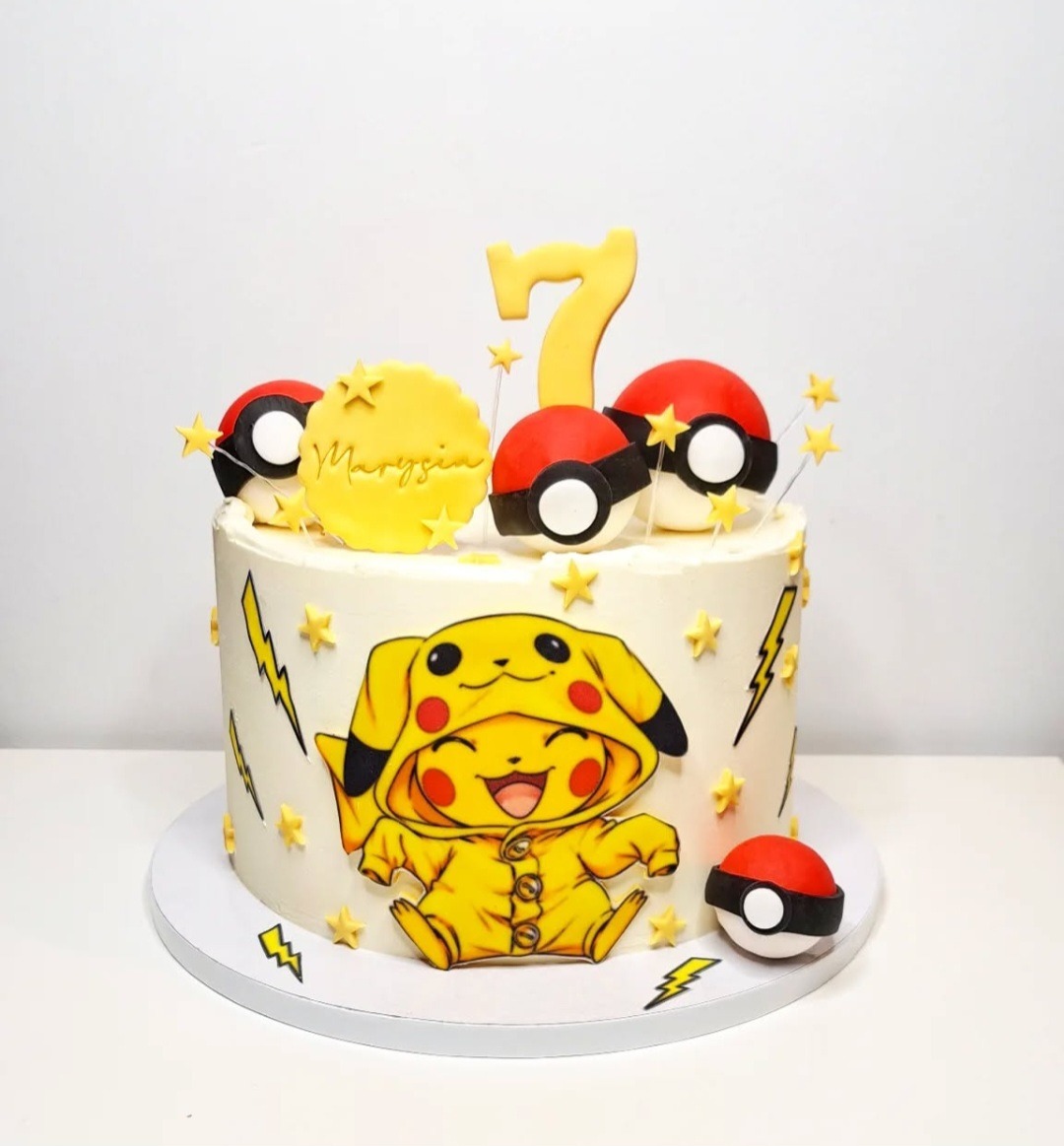 Tort urodzinowy z motywem Pikachu i Pokeballi, ozdobiony imieniem 'Marysia' i cyfrą '7', na białym tle.