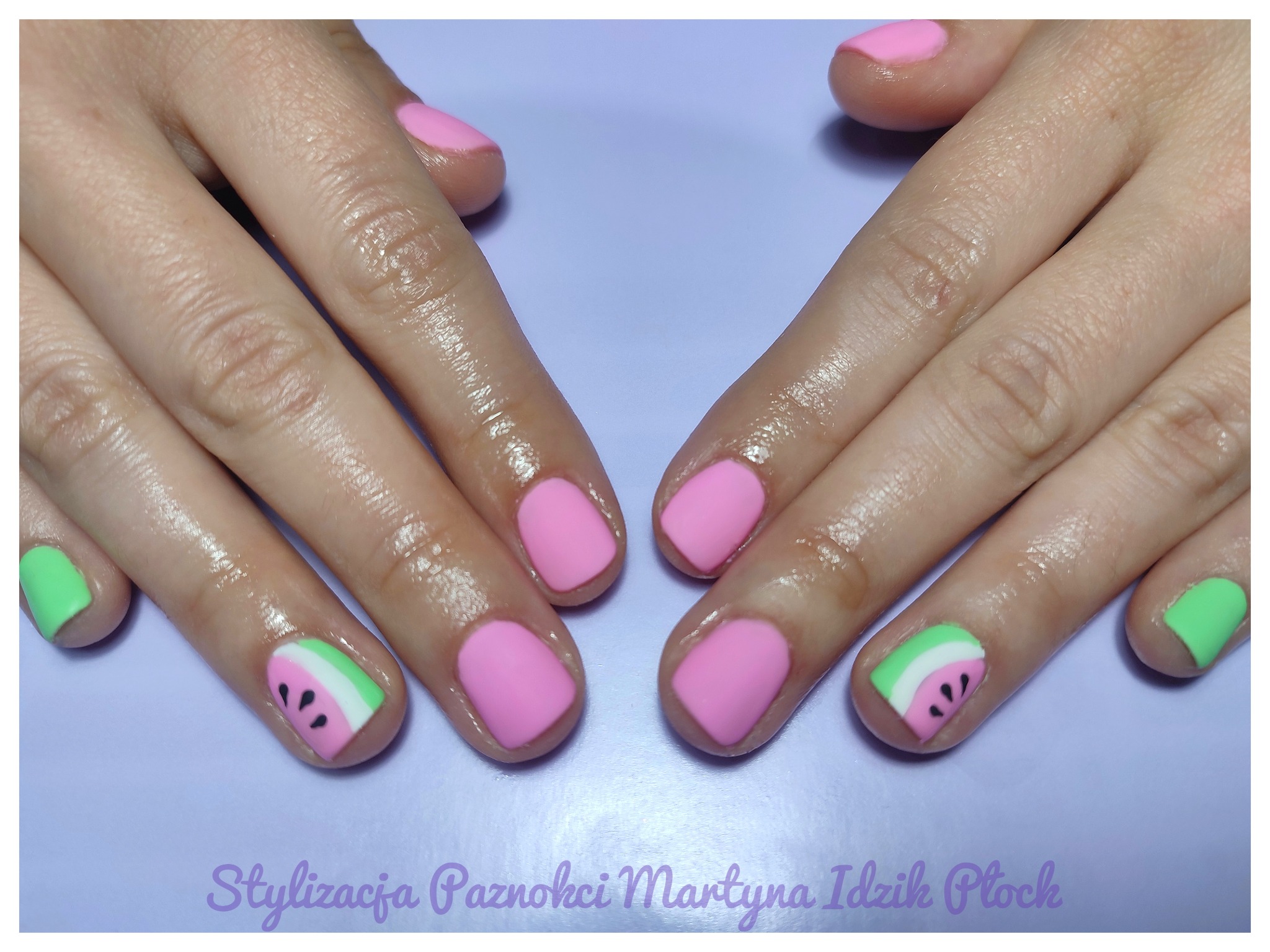 Dłonie z pomalowanymi paznokciami: różowe i z motywem arbuza, na fioletowym tle.