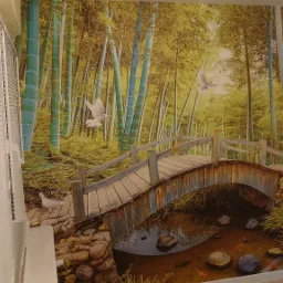 Fototapeta z motywem bambusowego lasu, drewnianego mostku nad strumieniem z rybkami koi i białych gołębi w locie, widoczna zza białych żaluzji.