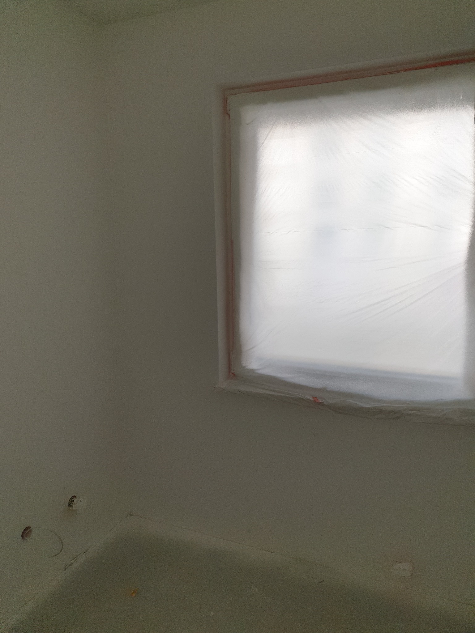 Pokój w trakcie malowania: zabezpieczone folią okno, świeżo pomalowane na biało ściany, widoczne puszki elektryczne.