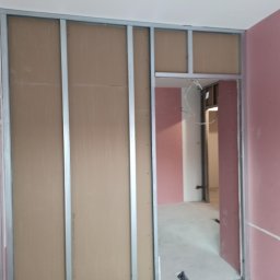 Usługi budowlano-wykończeniowe PIADA Adam Piaskowy - Konstrukcja szkieletowa z profili stalowych pod płyty gipsowo-kartonowe tworząca ścianę działową z otworem drzwiowym, widoczna instalacja elektryczna wewnątrz ściany.