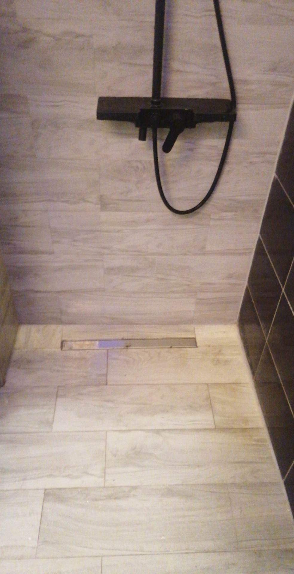 Wykończona strefa prysznicowa z odpływem liniowym i baterią natryskową w kolorze czarnym, płytki imitujące drewno, widok z góry.