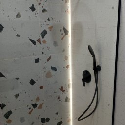 Zmuda Trzebiatowski - Wykończona kabina prysznicowa z czarną armaturą na tle płytek lastryko i podświetlaną listwą LED. Nowoczesny design łazienki.