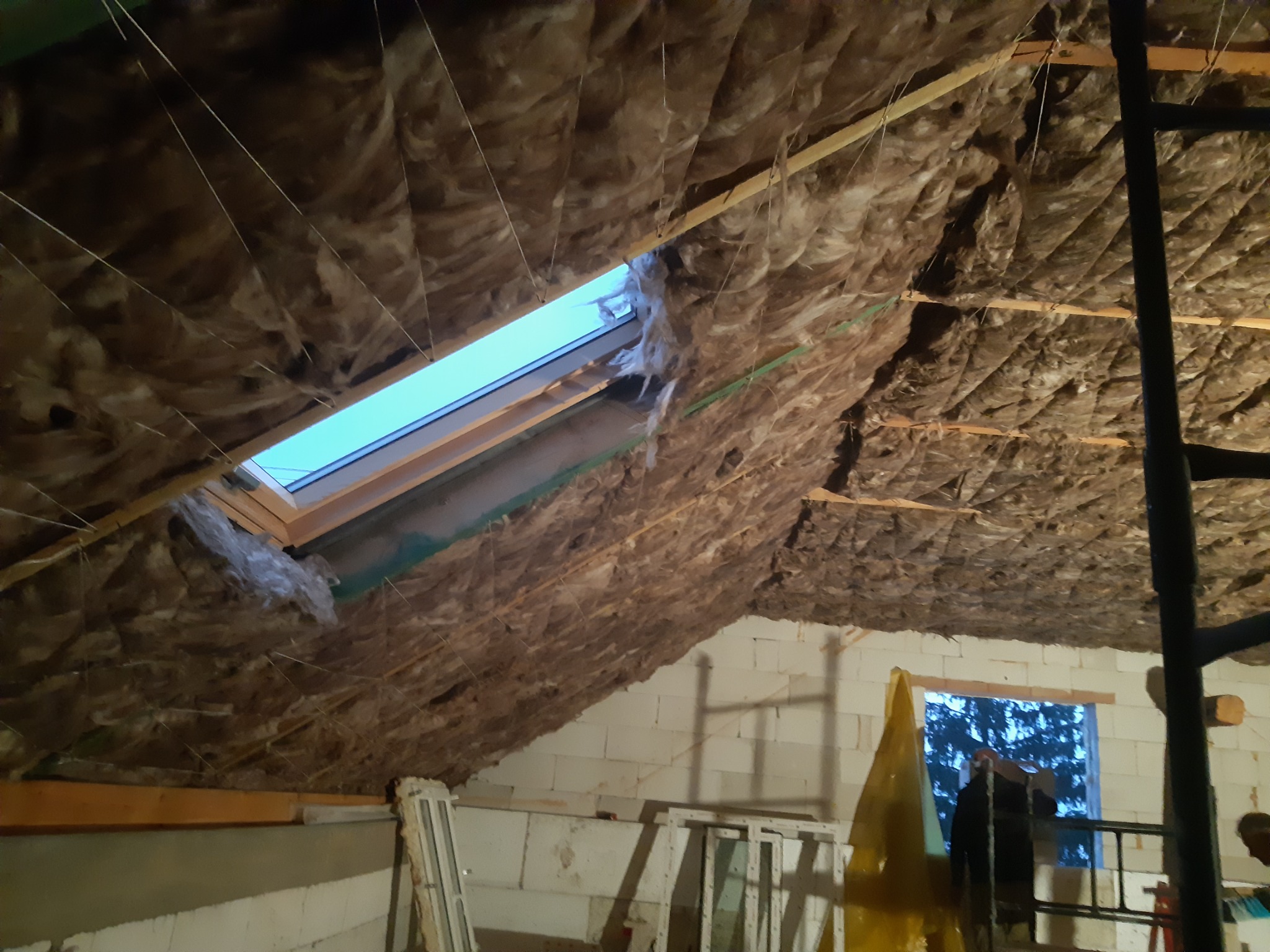 Ocieplenie poddasza wełną mineralną z widocznym oknem dachowym, konstrukcja drewniana i fragment ściany z białego pustaka