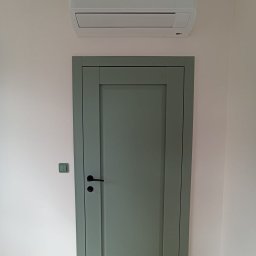 KLIMAVIP Rafał Nowicki - Biała jednostka wewnętrzna klimatyzacji Samsung Wind-Free Avant zamontowana nad zielonymi drzwiami w jasnym wnętrzu. Widoczne gniazdko i włącznik.