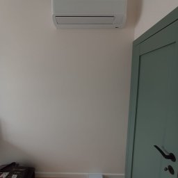 KLIMAVIP Rafał Nowicki - Biała jednostka wewnętrzna klimatyzacji Samsung Wind-Free Avant zamontowana na ścianie w jasnym pomieszczeniu, obok zielonych drzwi. Widoczny fragment podłogi.