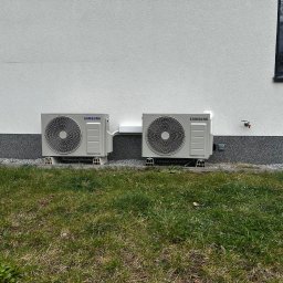 KLIMAVIP Rafał Nowicki - Dwa zewnętrzne agregaty klimatyzacji Samsung Wind-Free Avant, zamontowane na niskich podstawach przy ścianie budynku z oknem i trawnikiem. Widok z poziomu gruntu.