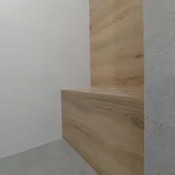 Nowoczesna łazienka z drewnianą półką wbudowaną w ścianę, białe płytki na ścianie i szare płytki na podłodze.