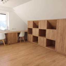 MEBLE-STYL DAWID ŁOPUSZYŃSKI - Pokój na poddaszu z drewnianą zabudową: regał z otwartymi półkami i biurko z szufladami, dwa białe krzesła, okno z widokiem na zieleń.