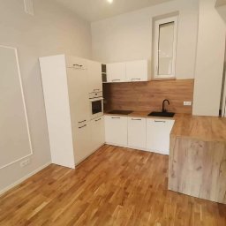 MEBLE-STYL DAWID ŁOPUSZYŃSKI - Nowoczesna kuchnia z białymi szafkami, drewnianym blatem i wyspą na parkiecie, minimalistyczny design.