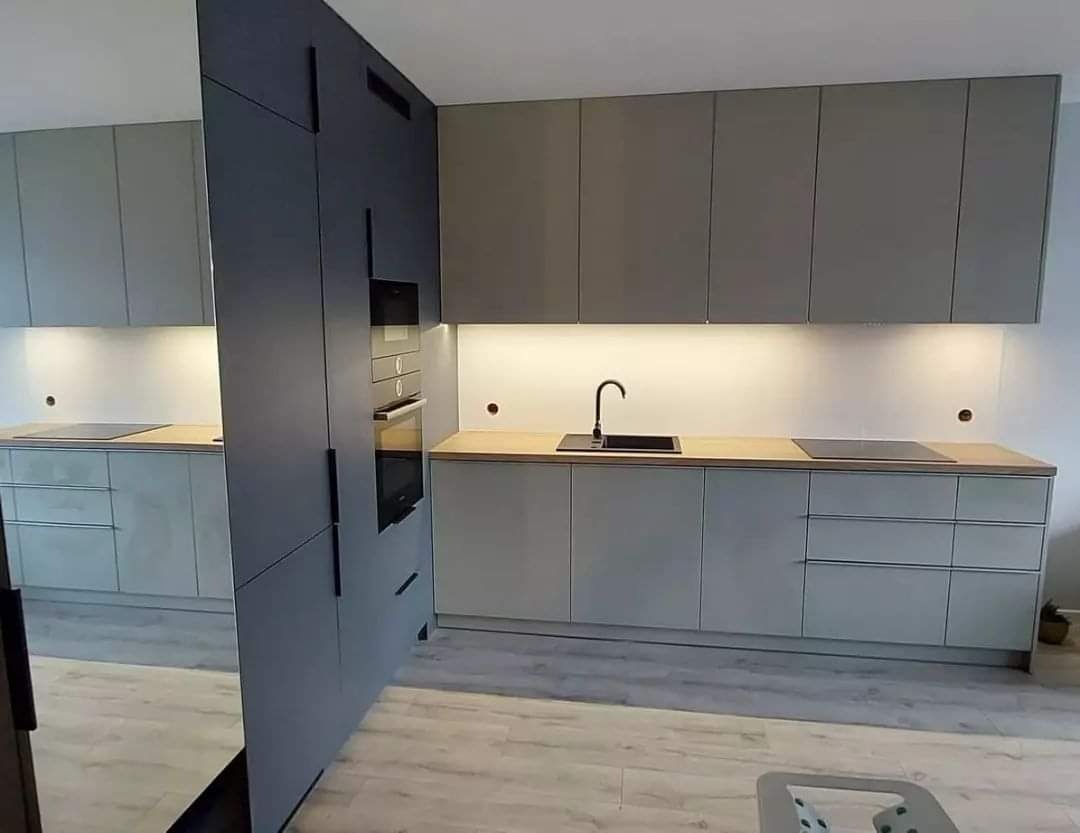 Nowoczesna kuchnia na wymiar z szarymi frontami szafek, drewnianym blatem i czarną armaturą, oświetlona ledowym światłem podszafkowym.