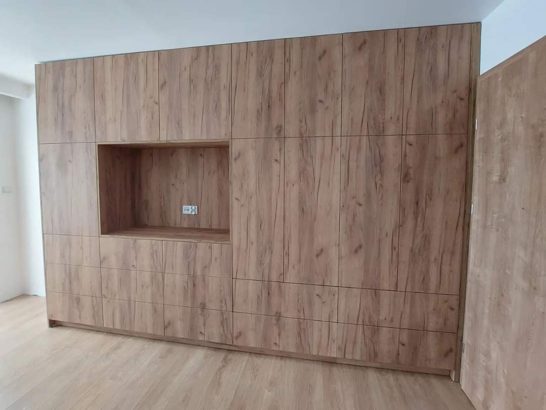 Duża szafa wnękowa z drewnopodobną okleiną, z otwartą wnęką na sprzęt RTV i gniazdkiem elektrycznym wewnątrz, dopasowana kolorystycznie do podłogi.