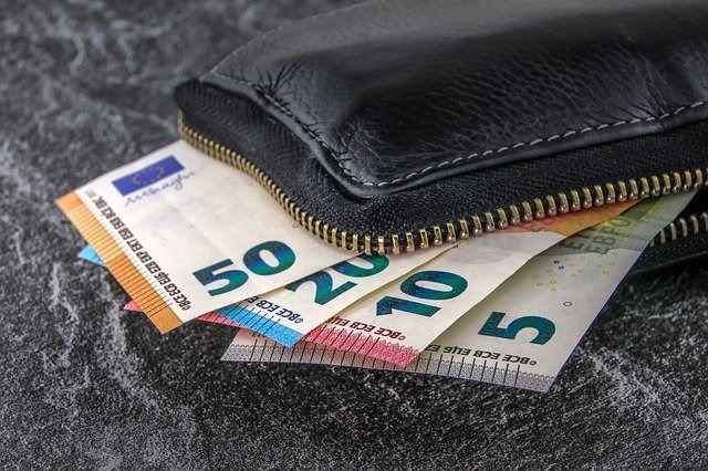 Częściowo otwarty czarny portfel z wysuwającymi się banknotami euro o nominałach 50, 20, 10 i 5 euro na szarym tle.